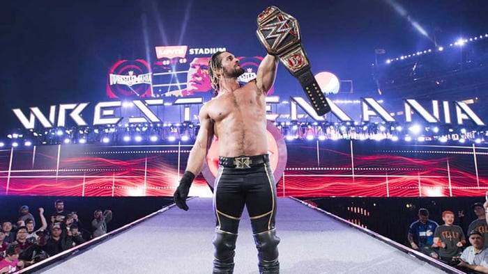 WWE Wrestler Seth Rollins holds up a title belt.