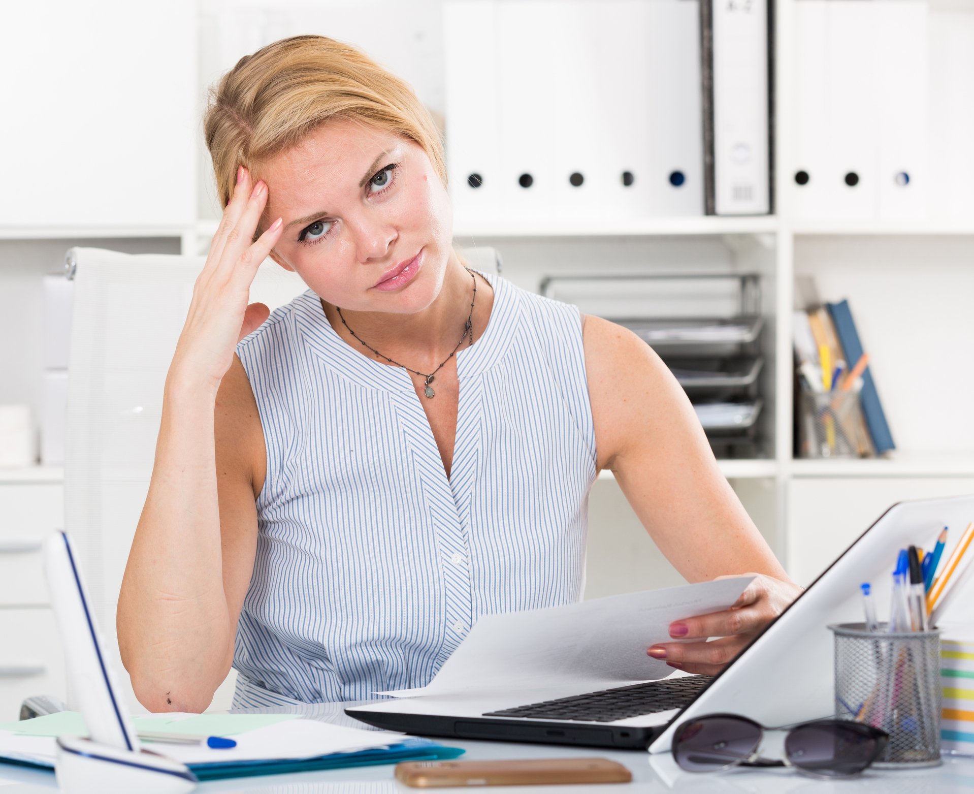 Woman looking sheepish at her desk, holding her head