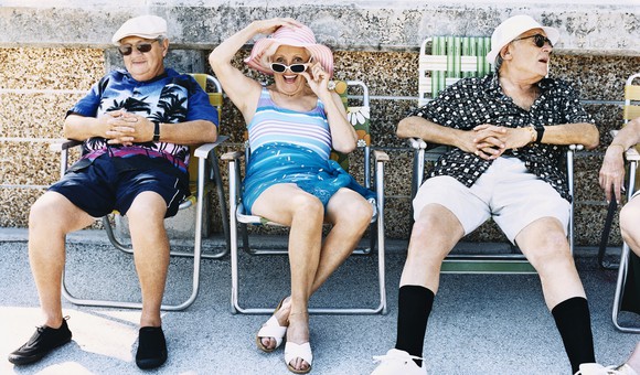 A group of retirees smiling and chatting in folding beach chairs.