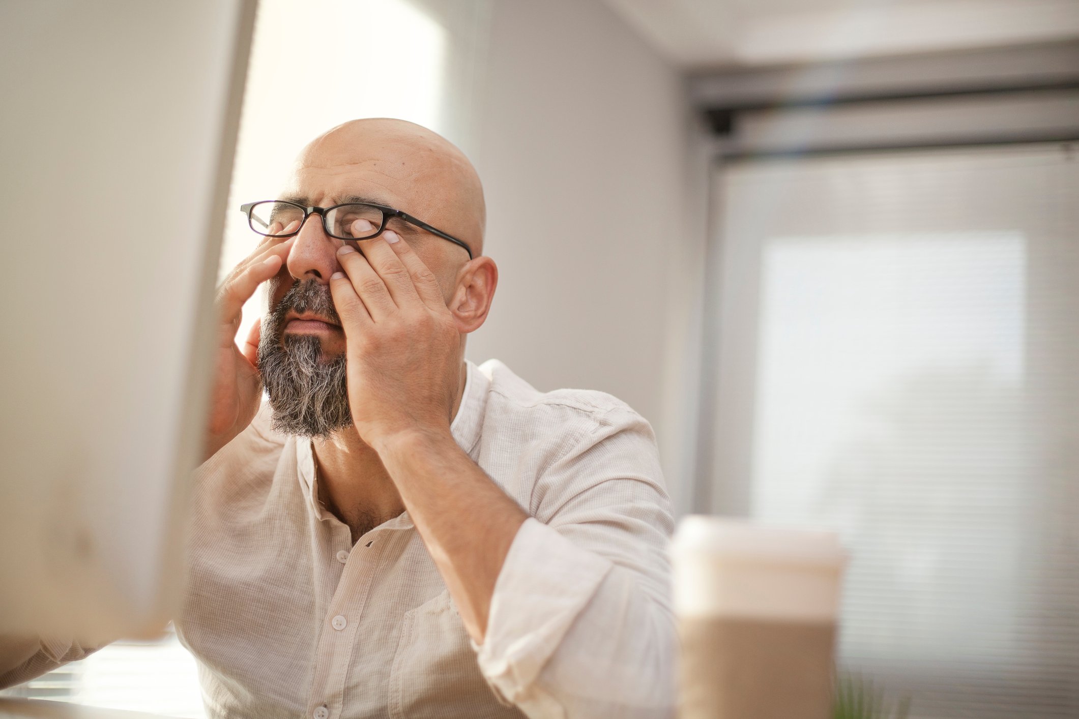 Man rubbing his eyes in front of a computer