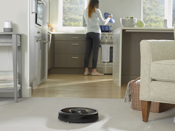 iRobot's Roomba 980 vacuum cleaning a floor with a woman doing dishes in the background