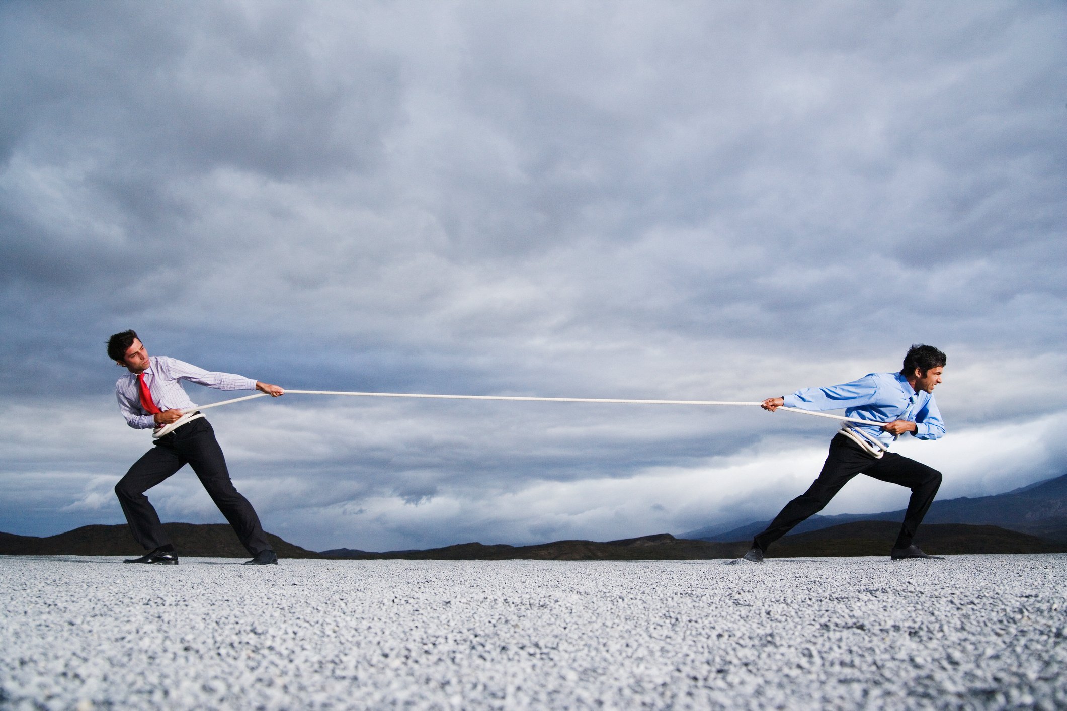 Two businessmen playing tug of war with a rope.