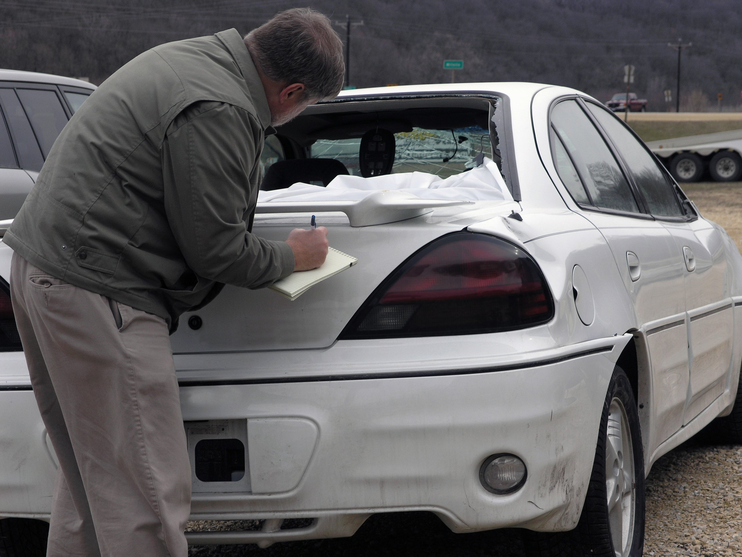 Man writing on a notepad on a car that's just been in an auto accident. 