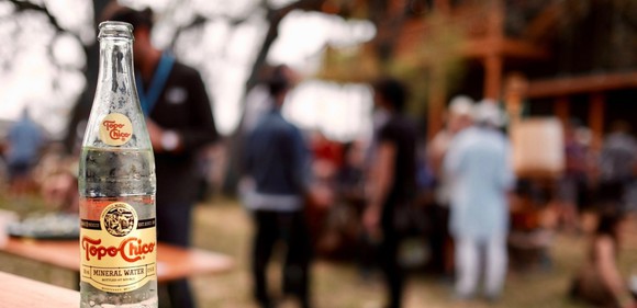 A battle of Topo Chico with a blurry group of people in the background.