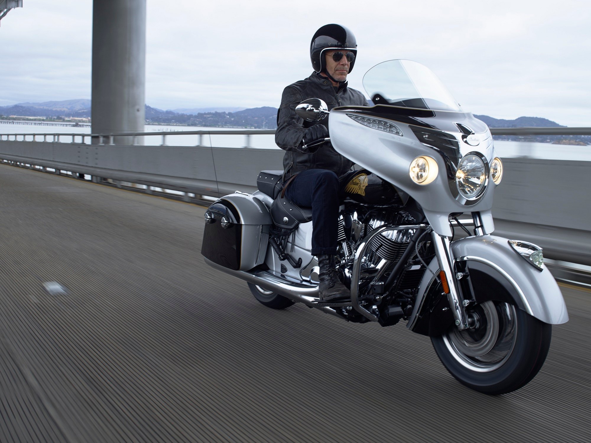 A man riding a Polaris Indian motorcycle over a bridge.