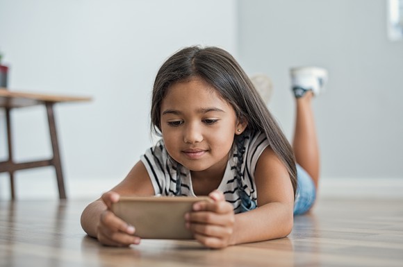 A young girl looks at the screen of a mobile phone.