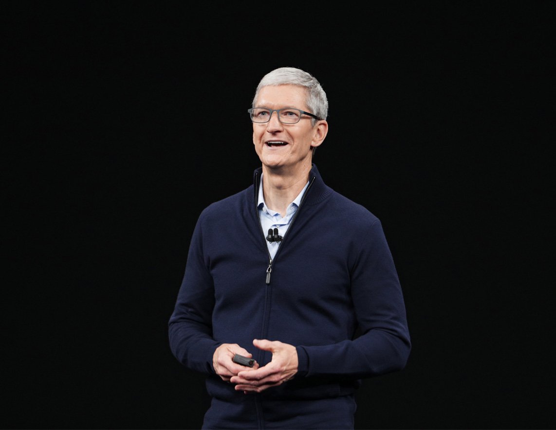 Cook is standing before a black backdrop on stage at an Apple event.