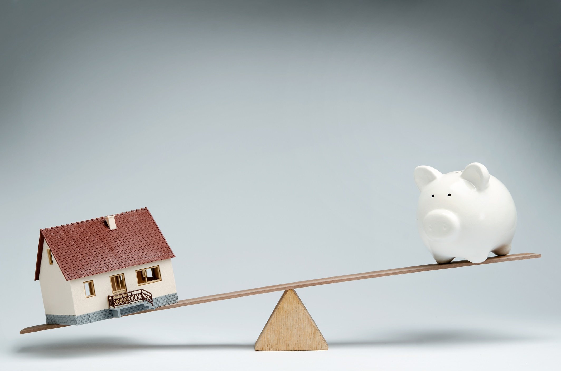Model home and piggy bank balancing on a fulcrum.