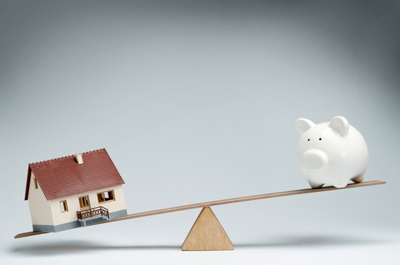 Model home and piggy bank balancing on a fulcrum.
