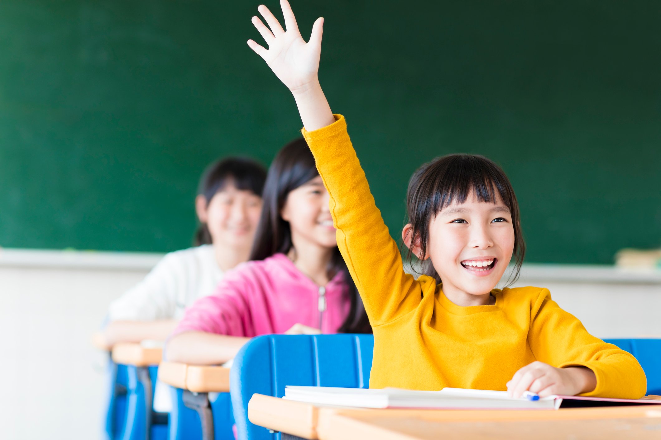 An Asian girl raising her hand in a classroom