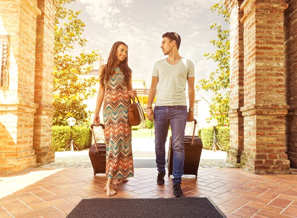 Young couple walking into a hotel with rolling suitcases