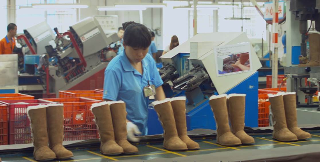 Assembly line with Uggs and a female worker wearing a blue shirt overseeing them.