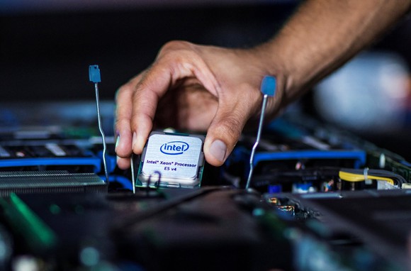 A hand holding an Intel Xeon E5 processor over a motherboard.