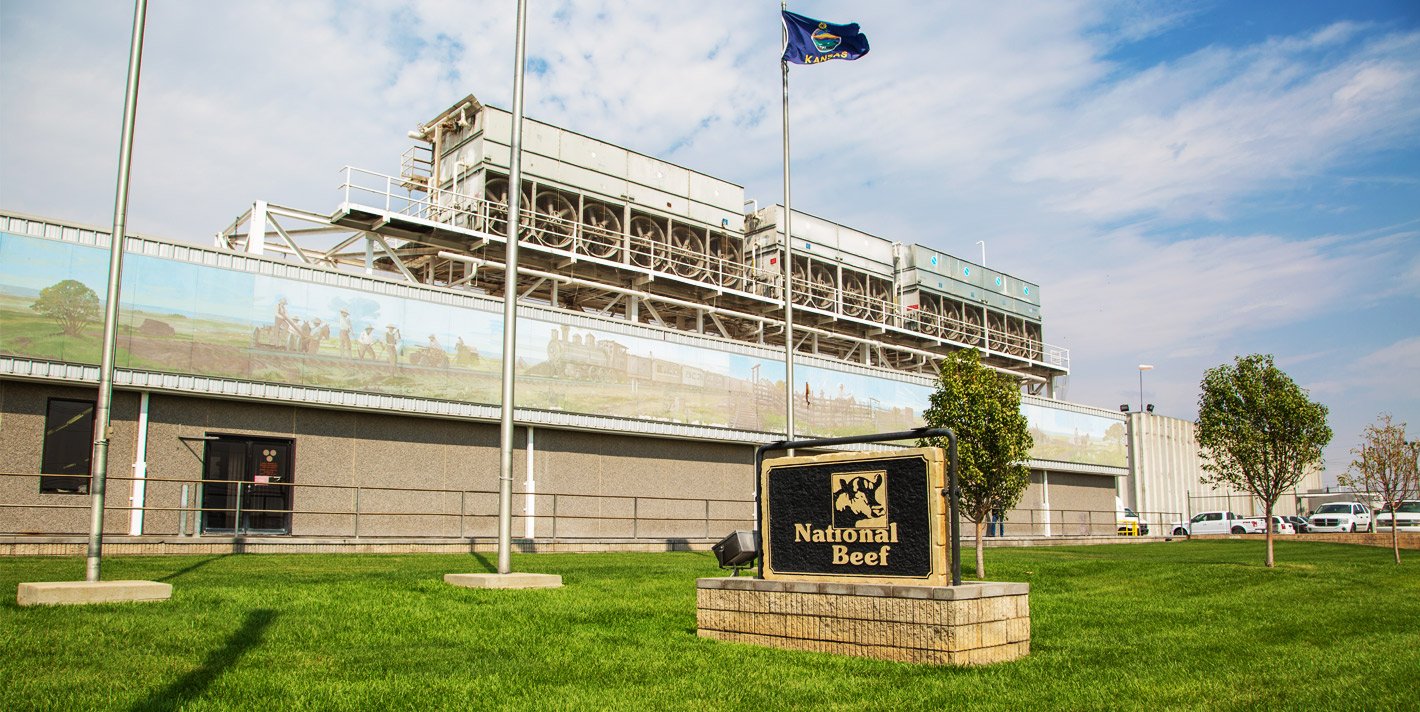 Factory headquarters building for National Beef, with green lawn, flag poles, and a couple of trees in front.