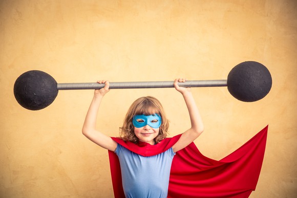 Child in super hero costume lifting foam barbell.