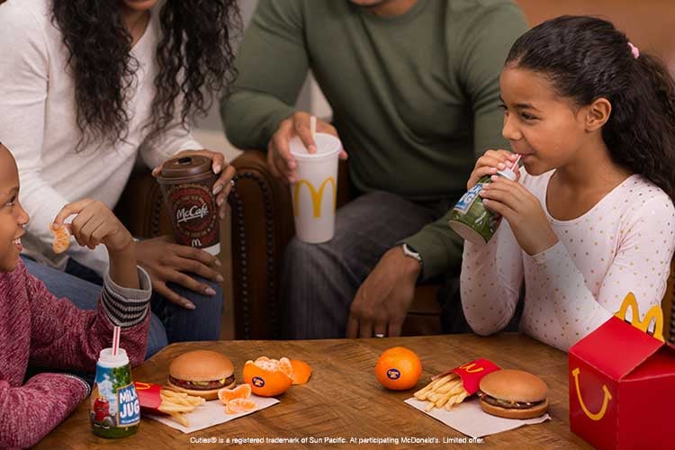 Children gathered around a table with parents eat a McDonald's kids meal offering.