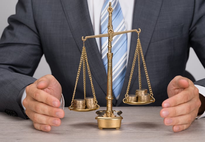 A businessperson sitting in front of a scale that is weighing two sets of coins.