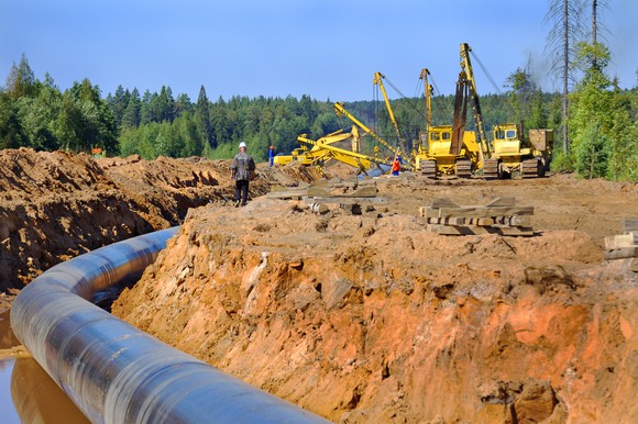 Pipeline under construction with cranes in the background.