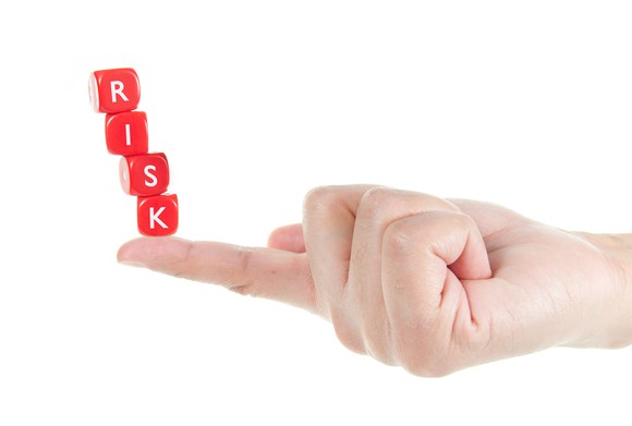Red blocks spelling out risk balanced on a person's index finger