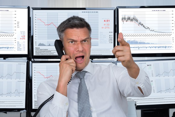 Angry man in front of six monitors displaying stock charts.