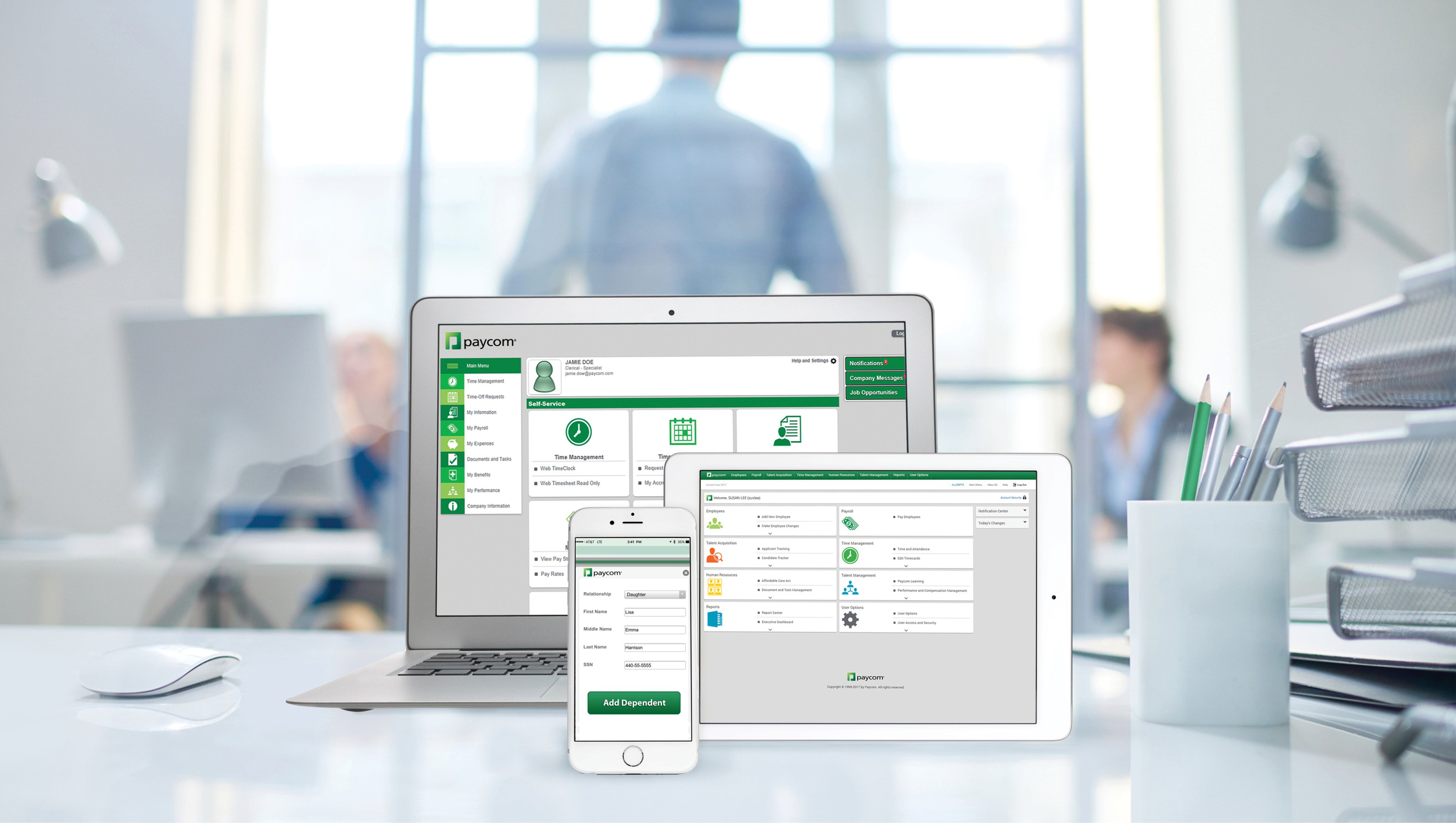 A laptop, tablet, and a phone showing various Paycom Software screens on an office desk