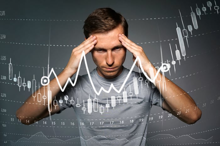 Man with hands on forehead standing behind stock chart