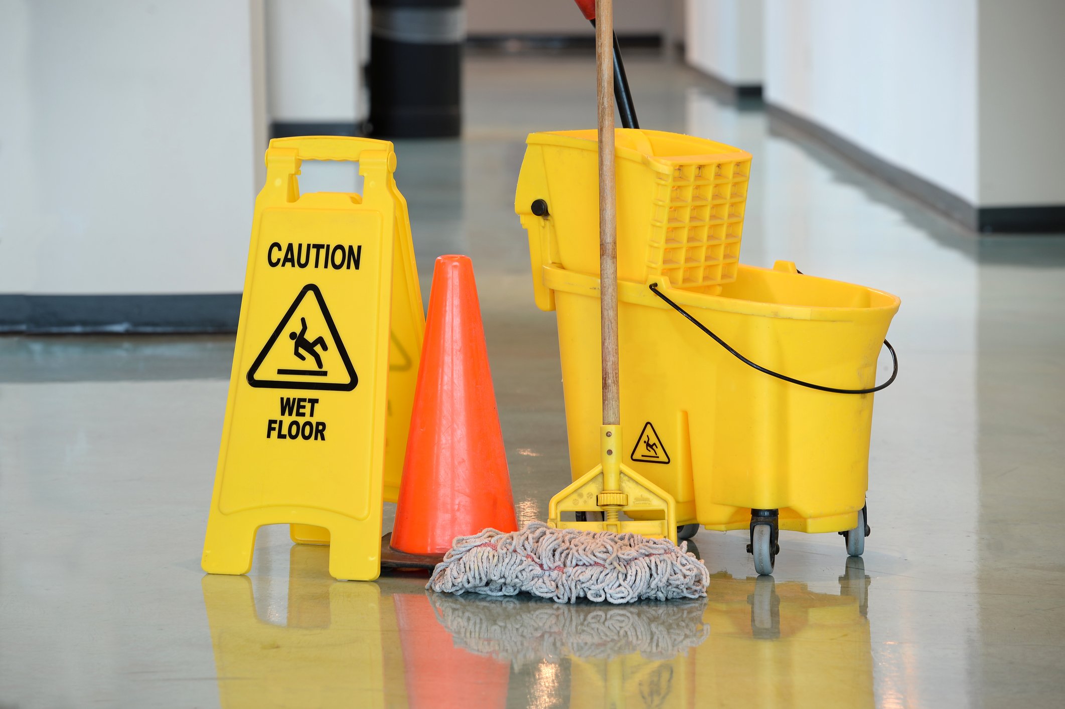 Yellow bucket and mop on floor next to a "caution" sign and orange cone.
