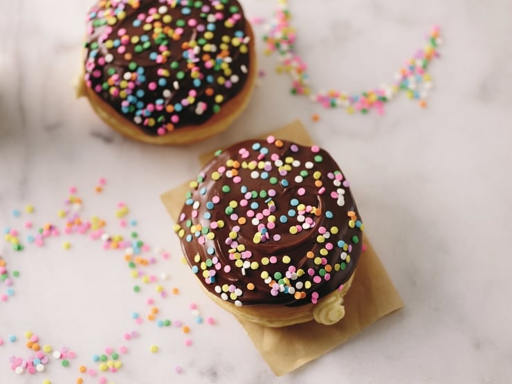Two chocolate-frosted "cake batter" doughnuts topped with sprinkles on marble counter. 