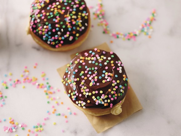Two chocolate-frosted "cake batter" doughnuts topped with sprinkles on marble counter. 