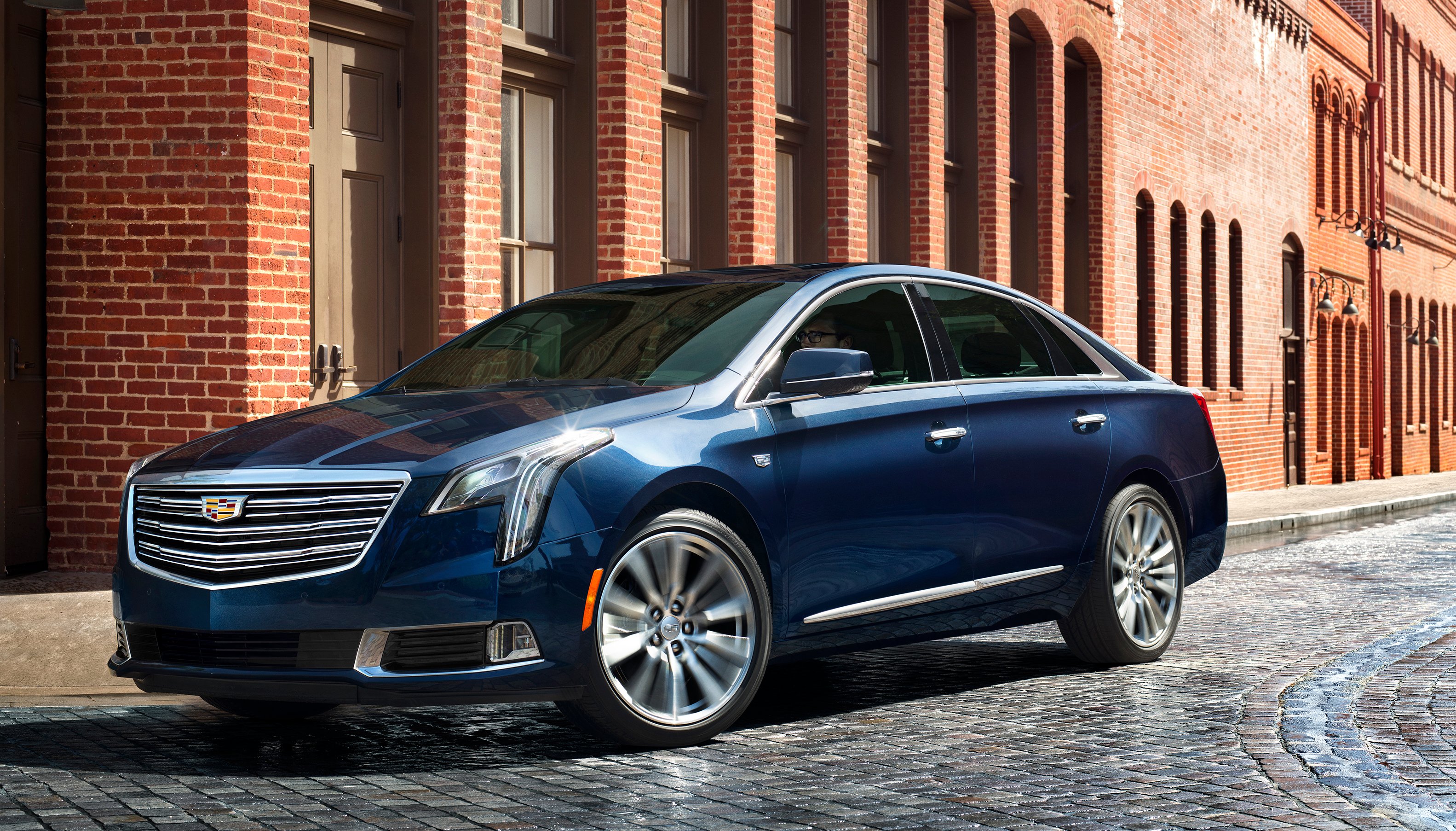 A dark blue Cadillac XTS sedan parked on a cobblestone city street.