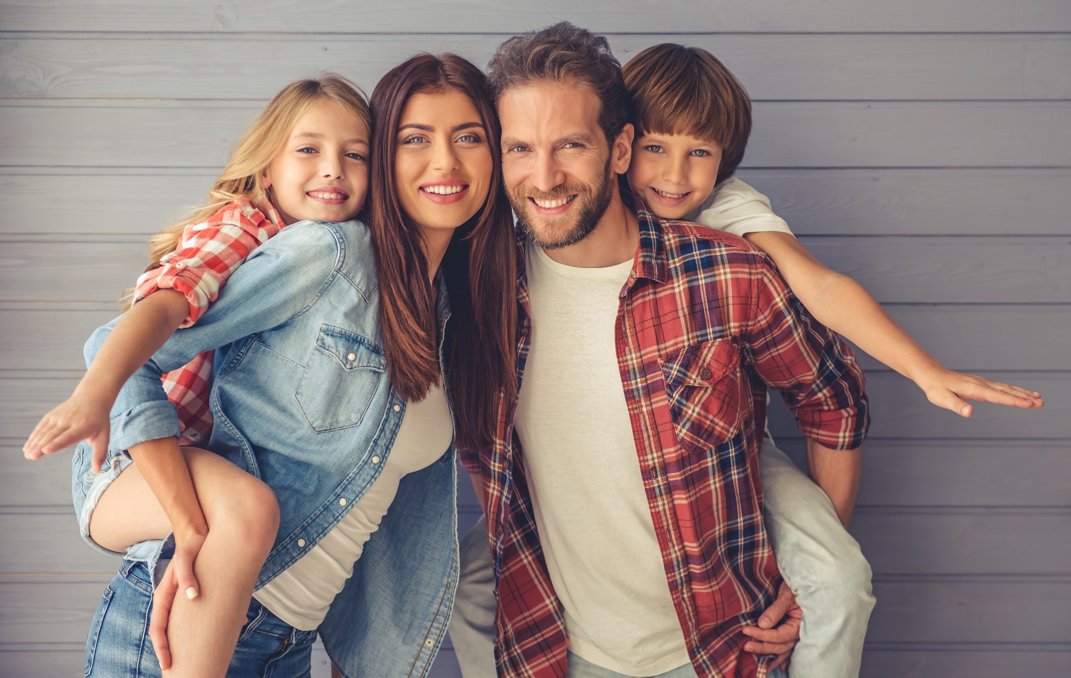 Woman holding girl on her back next to man holding boy on his back