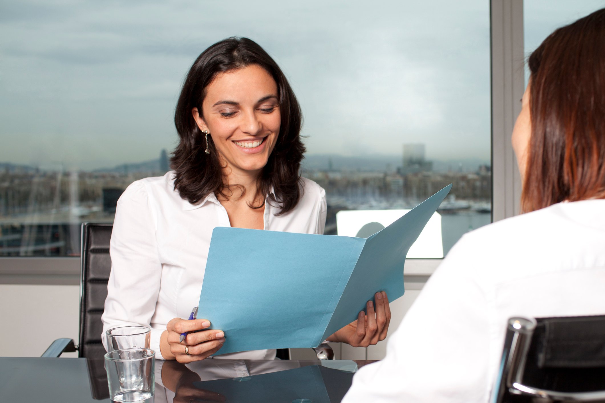 Professional woman reading a folder while sitting across from another woman