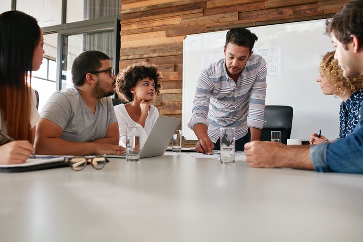 A group of people in casual clothing having a discussion around a white table.