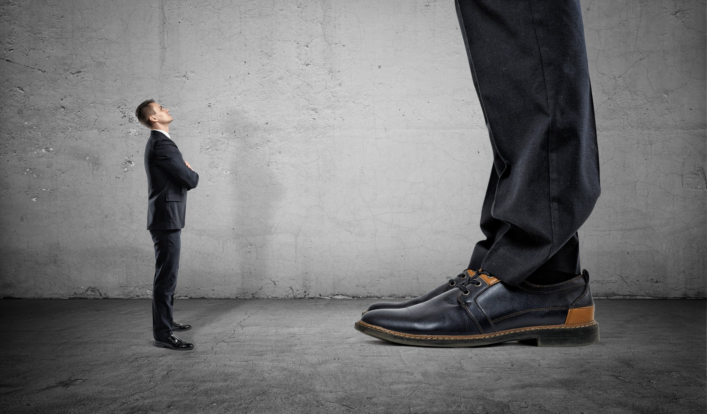 A small man in a suit looks up at a giant, whose feet and lower legs only can be seen.