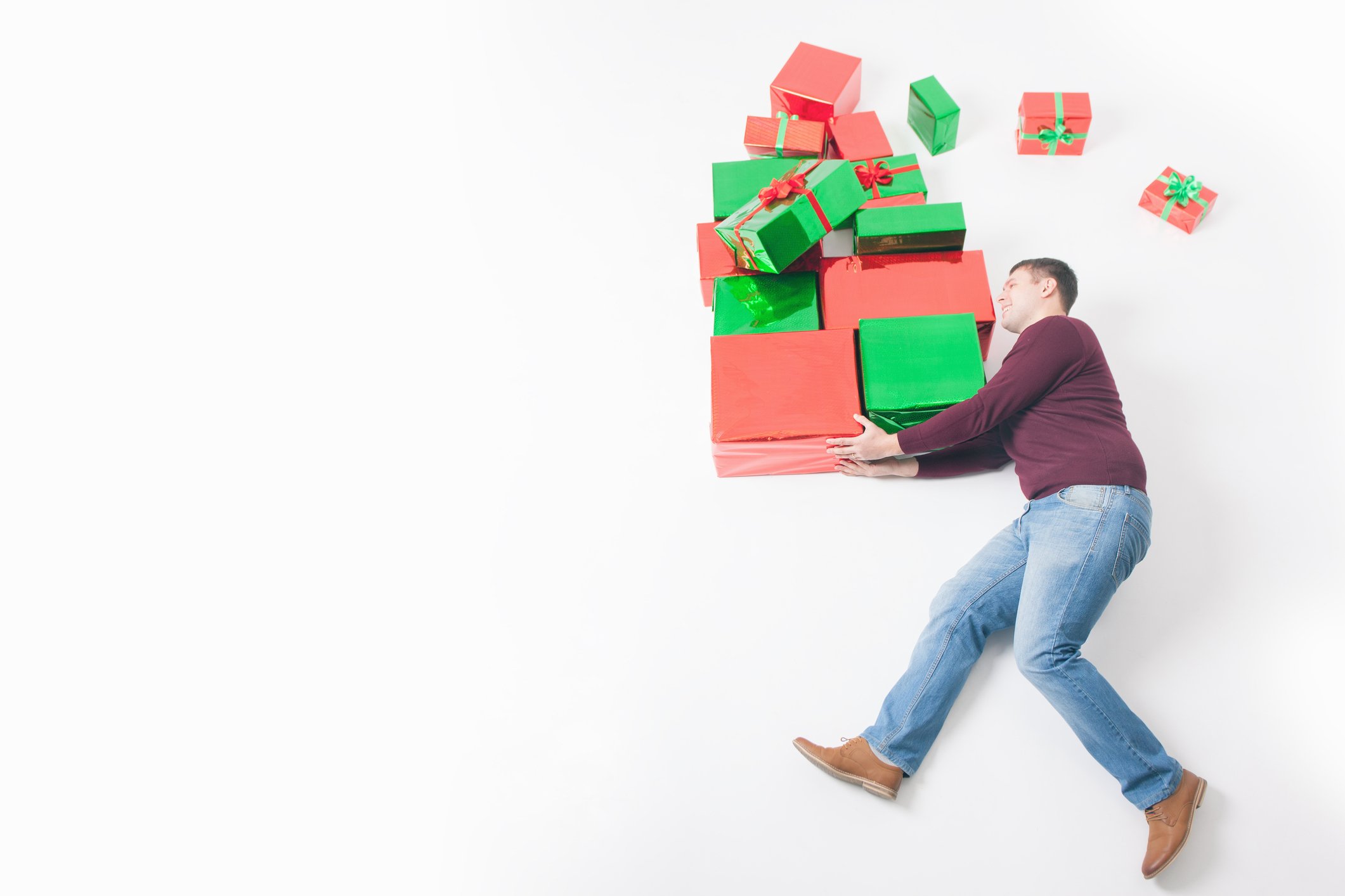 A man carries a huge load of wrapped presents in his arms, with several packages flying off the pile.