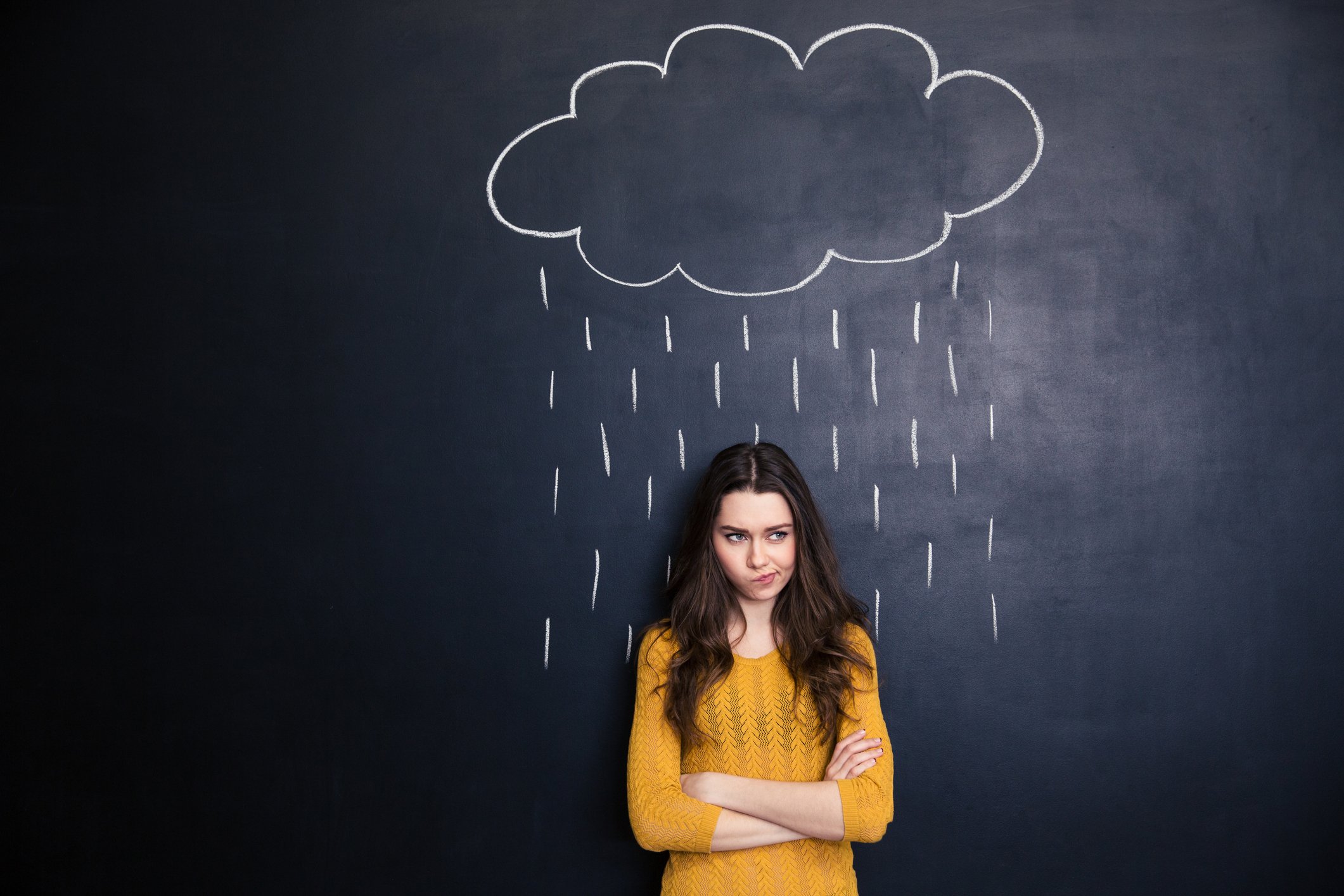 Woman standing in front of chalkboard with rain cloud over her head.