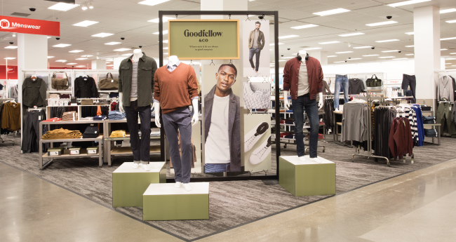 An in-store display of one of Target's new brands, Goodfellow and Co. Several men's outfits are displayed in front of a banner with a male model wearing jeans, a white T-shirt, and a sweater jacket.