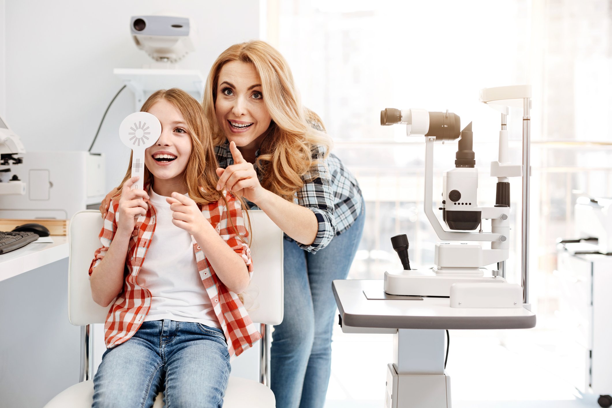 A child and her mother smiling as she gets an eye exam.