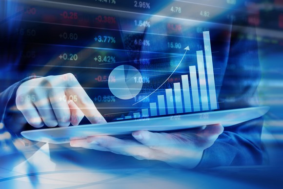 A person points at a tablet showing a rising column bar chart.