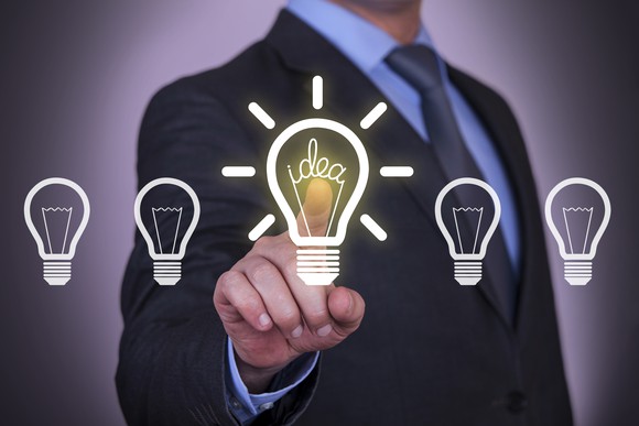 A man in a suit points at a lit up light bulb in a row of light bulbs.