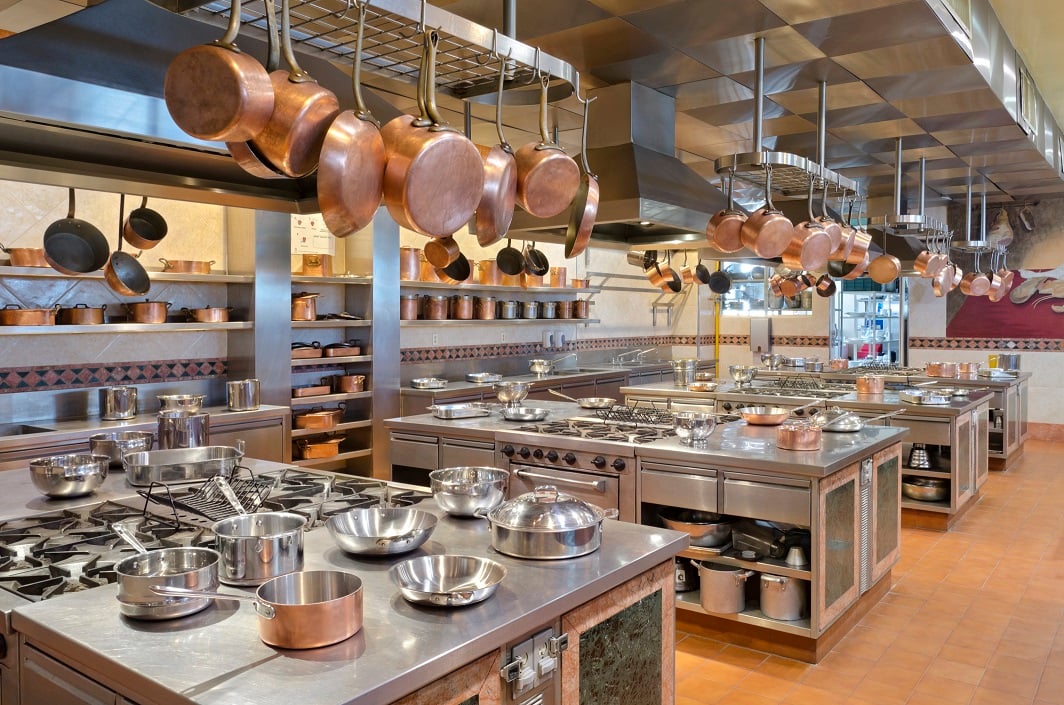 Commercial kitchen with pans hanging from the ceiling and a full array of counters, equipment, stoves, and ovens