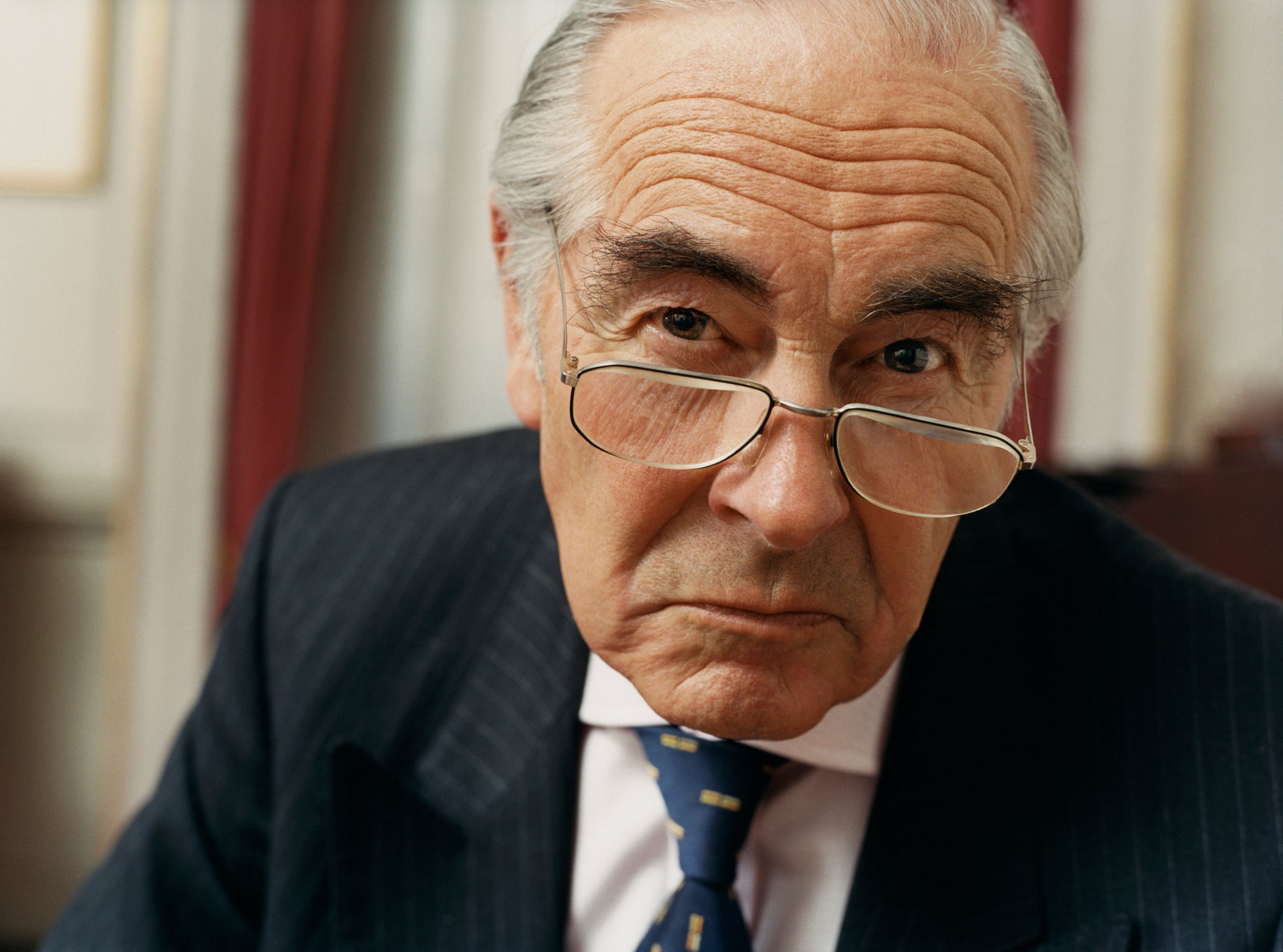 A wealthy elderly man in a suit with an annoyed look on his face. 