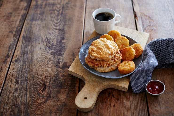 Cajun biscuit, Bo' rounds tater tots, and coffee arranged on a plate on wood table.