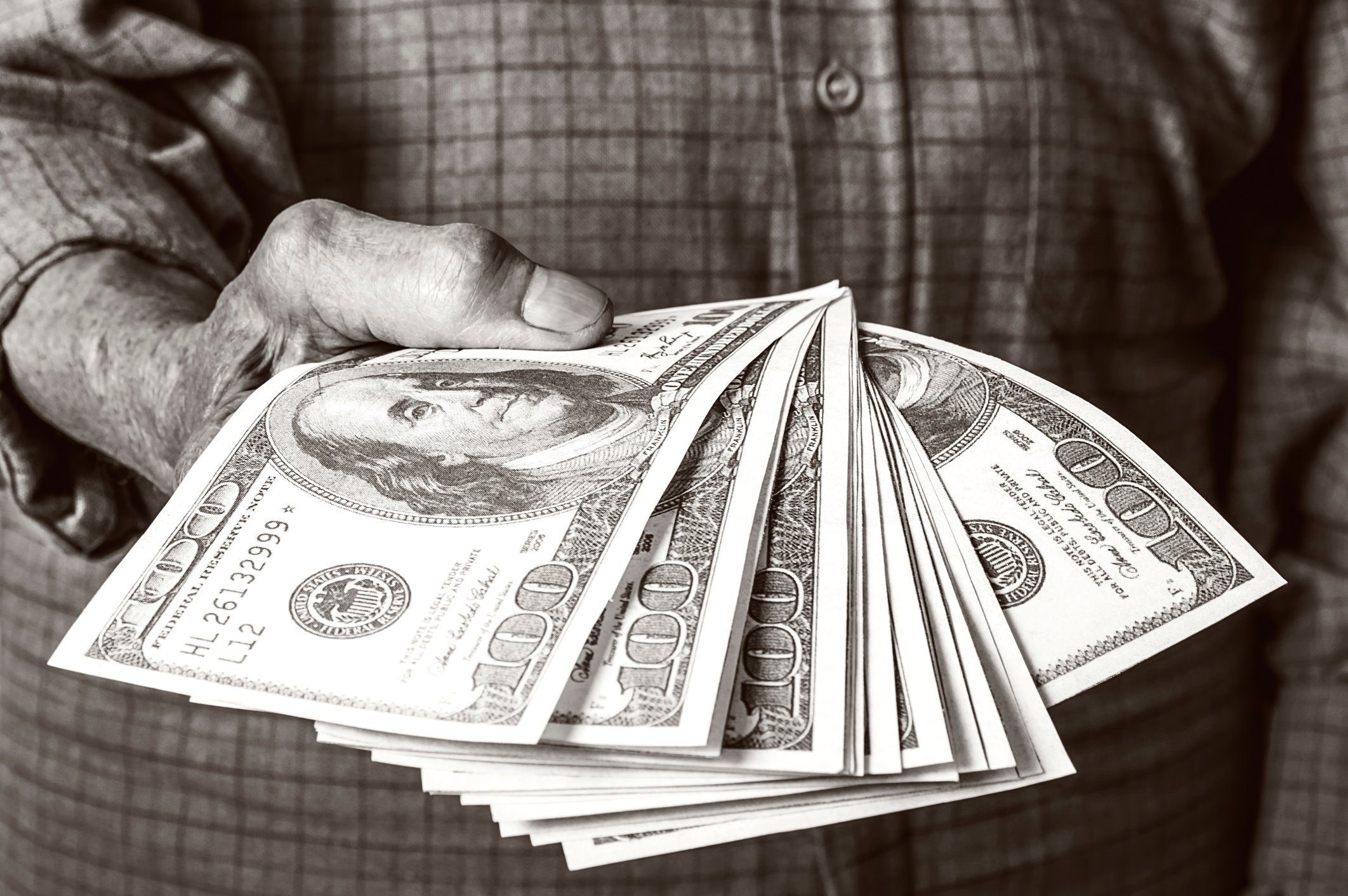A man holding a fanned stack of hundred dollar bills.