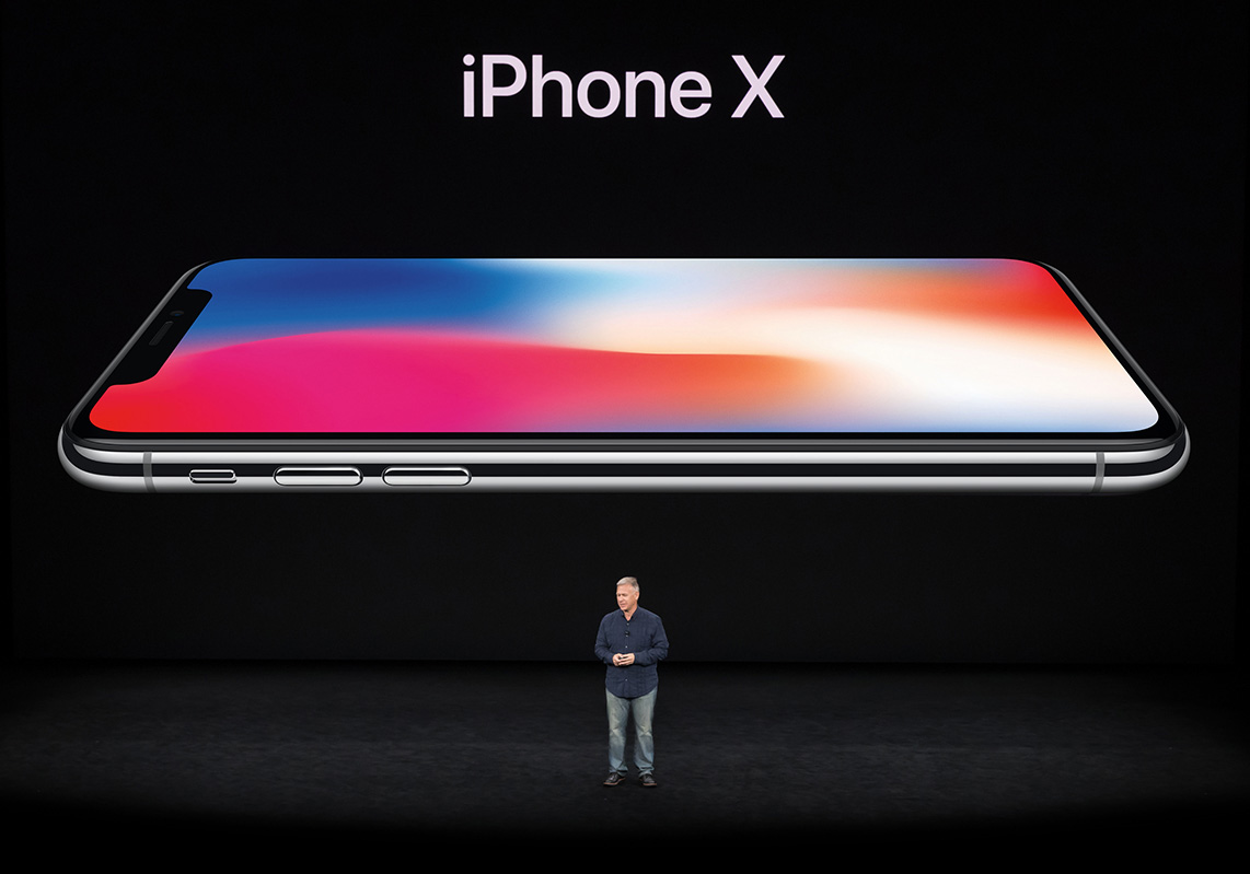 Apple marketing chief Phil Schiller standing on stage with an image of the iPhone X projected behind him.