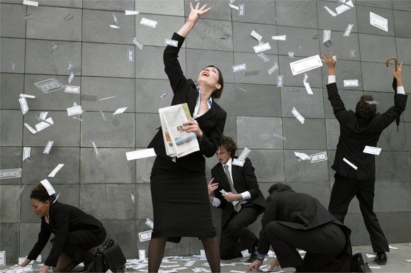 Cash money raining down on happy people in business attire.