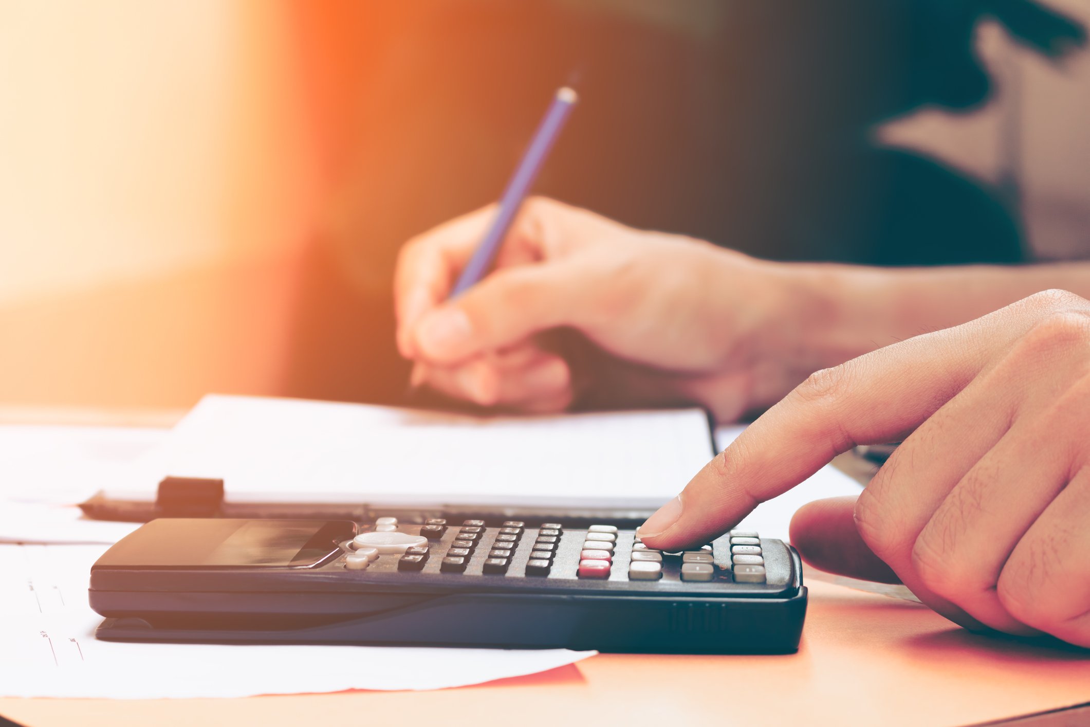 A person works a calculator with one hand and holds a pencil in the other.
