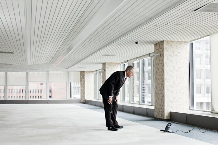 Older businessman staring at a phone in an empty office building