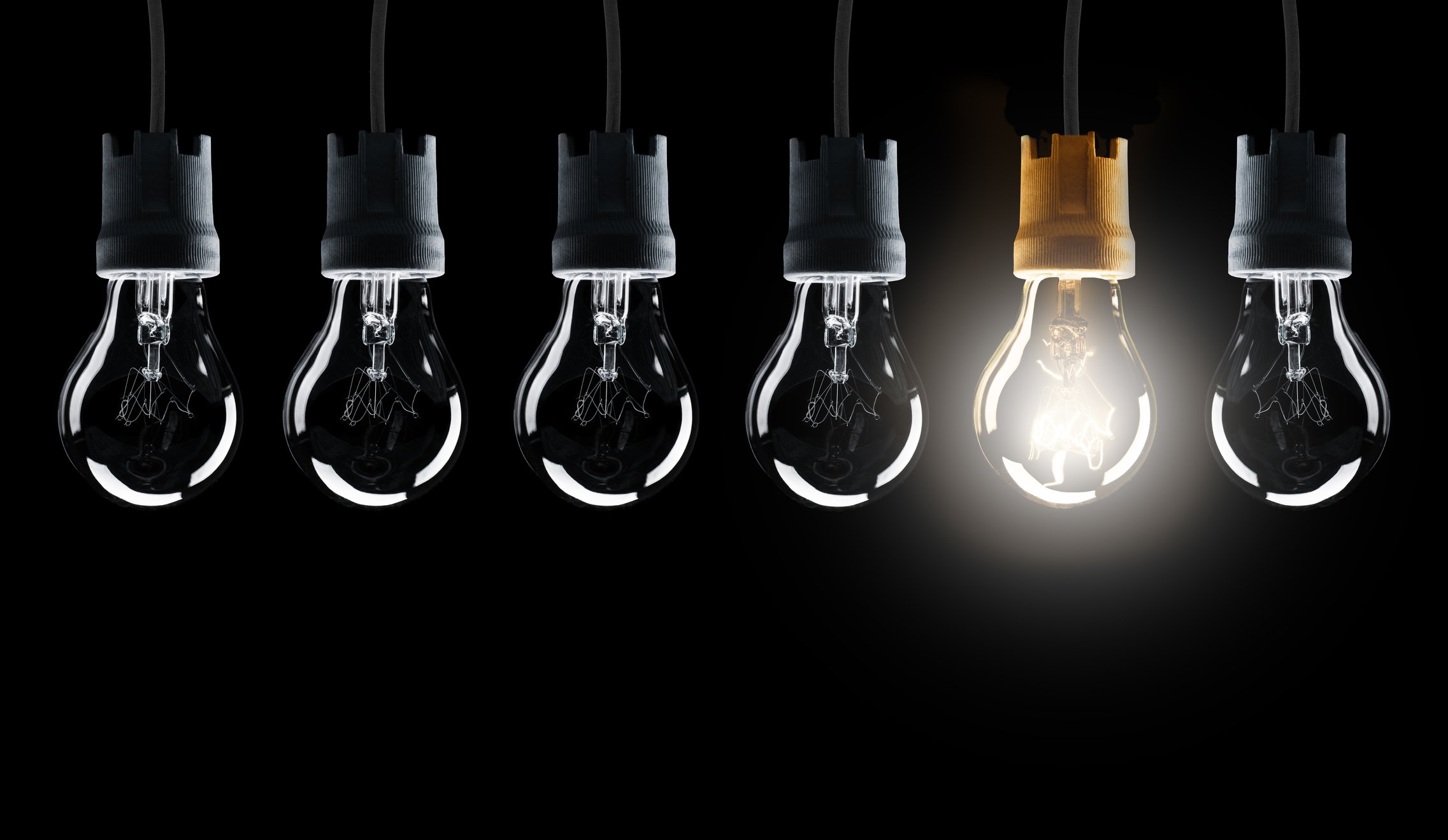 A row of six hanging light bulbs with the fifth lit.
