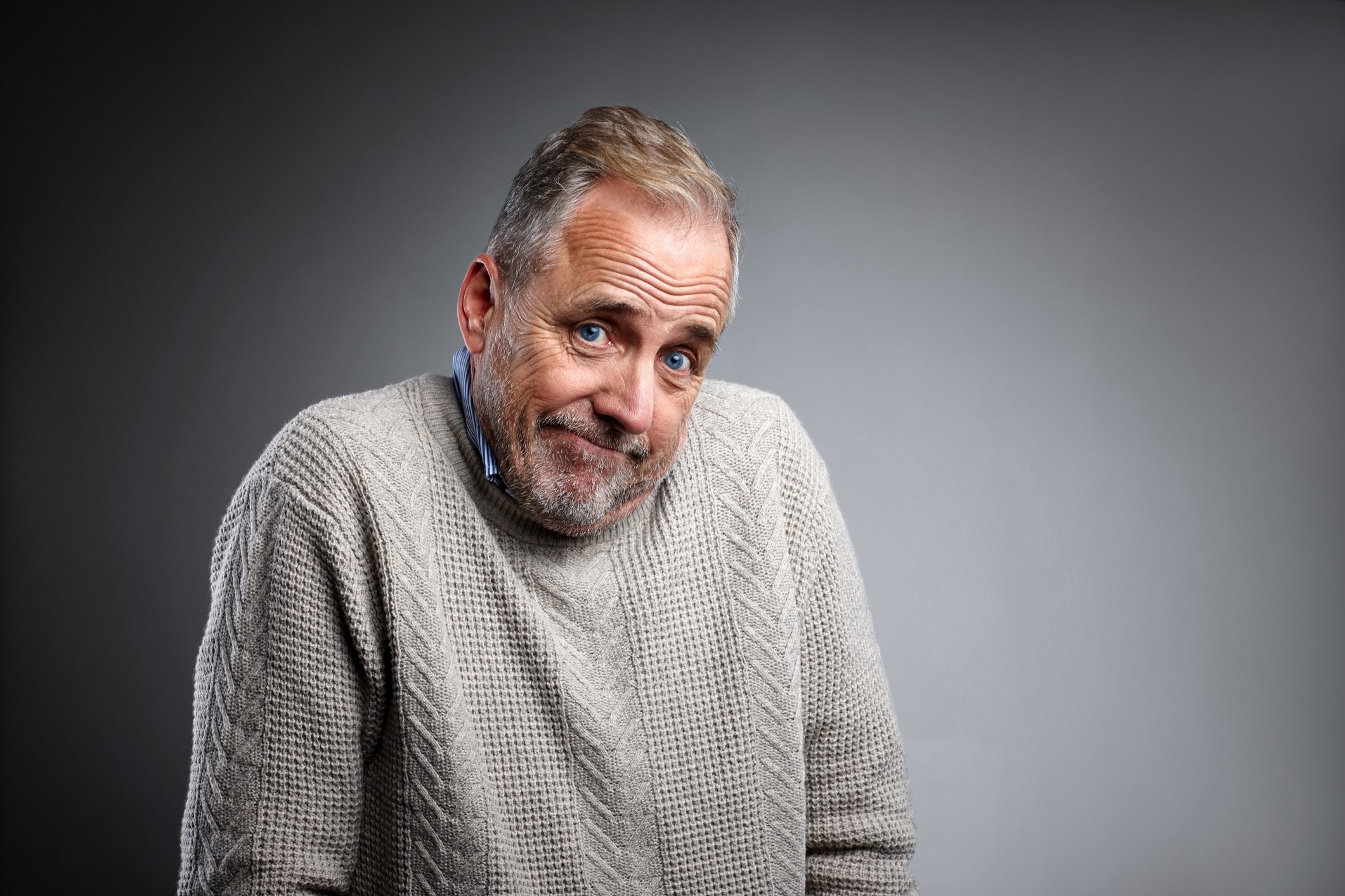 An elderly man shrugging his shoulders while smirking. 